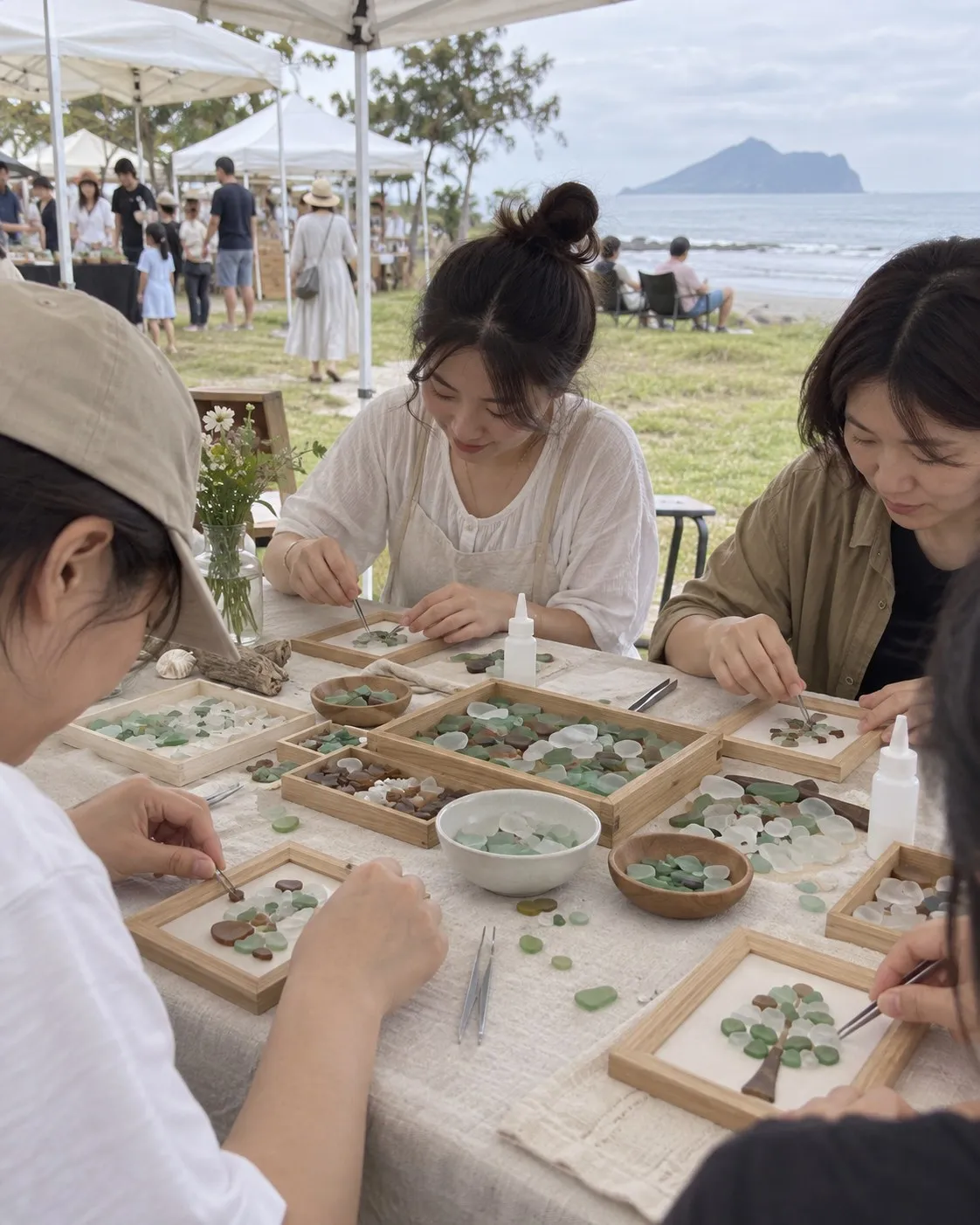 帳篷下的長桌上，幾個人用鑷子把綠色、白色、咖啡色的海玻璃貼進小木框，桌上有一盒盒分好色的海玻璃。